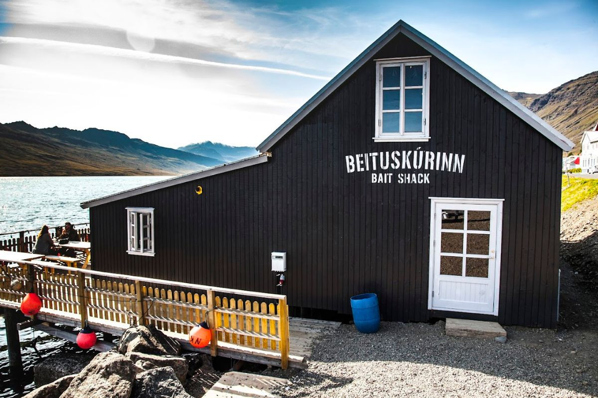 The black wooden exterior of Beituskúrinn Bait Shack restaurant by the water in Neskaupstaður, recommended by Handpicked Iceland.