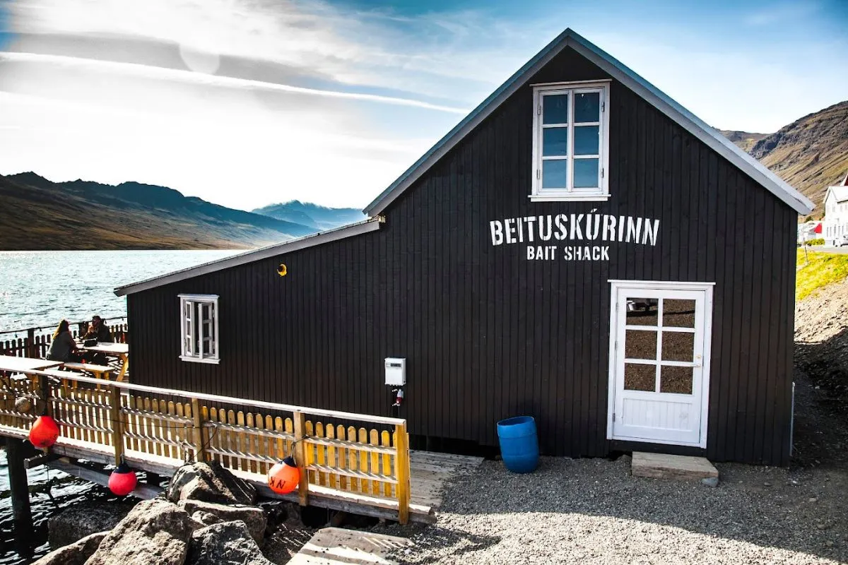 The black wooden exterior of Beituskúrinn Bait Shack restaurant by the water in Neskaupstaður, recommended by Handpicked Iceland.