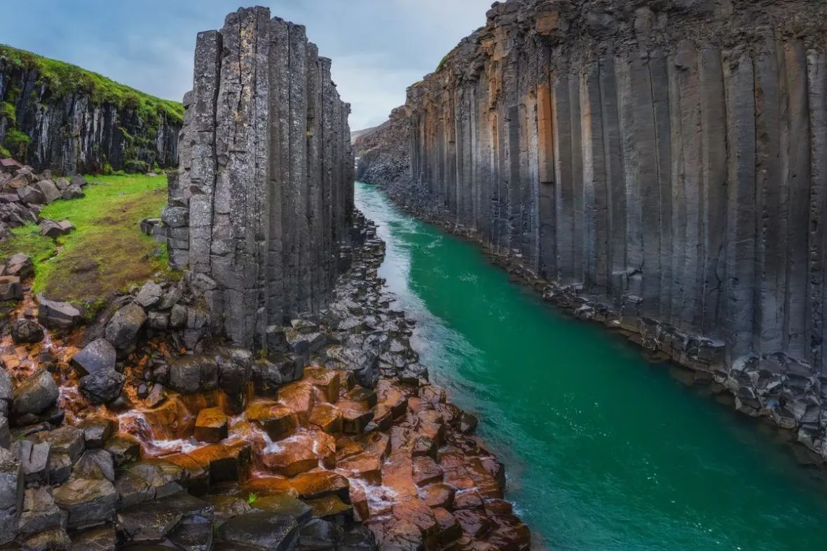 View of the turquoise waters flowing through the dramatic basalt columns of Stuðlagil Canyon with Tinna Adventure.