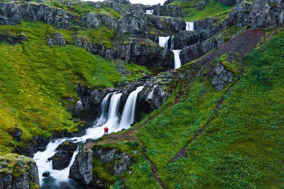 View of a multi-tiered waterfall cascading down a lush green hillside with Tinna Adventure.