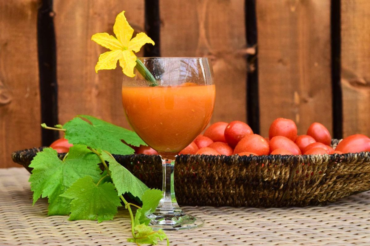 Fresh tomato cocktail garnished with a yellow flower next to a basket of ripe tomatoes at Friðheima.